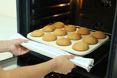 Photo of Woman taking cupcakes out of oven indoors, closeup