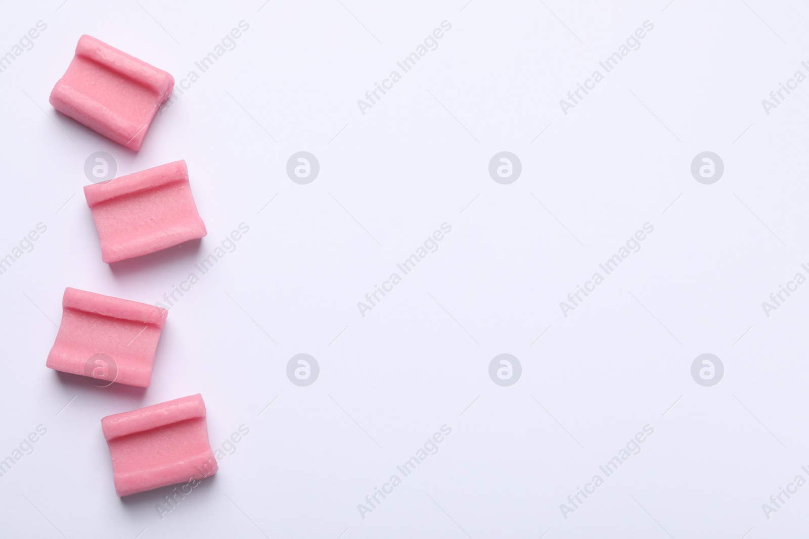 Photo of Tasty pink chewing gums on white background, flat lay. Space for text