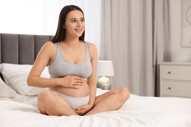 Photo of Beautiful pregnant woman in comfortable maternity underwear on bed at home, space for text