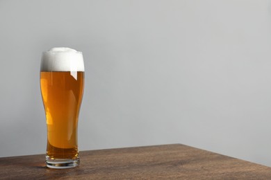 Photo of Glass of tasty beer on wooden table. Space for text