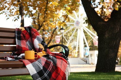 Photo of Wooden bench with cup of drink and plaid in park on autumn day. Space for text