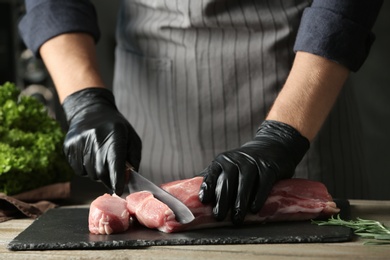 Man cutting fresh raw meat on wooden table, closeup