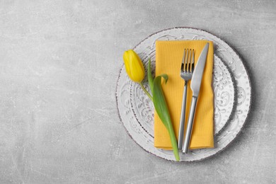 Photo of Festive table setting with tulip and cutlery on light grey background, top view with space for text. Easter celebration