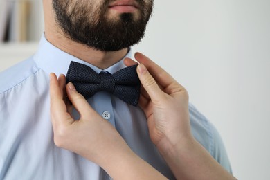 Photo of Woman adjusting bow tie to man indoors, closeup