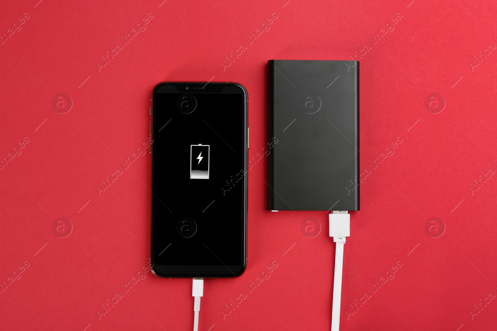 Photo of Mobile phone charging with power bank on red background, flat lay