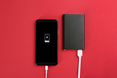 Mobile phone charging with power bank on red background, flat lay