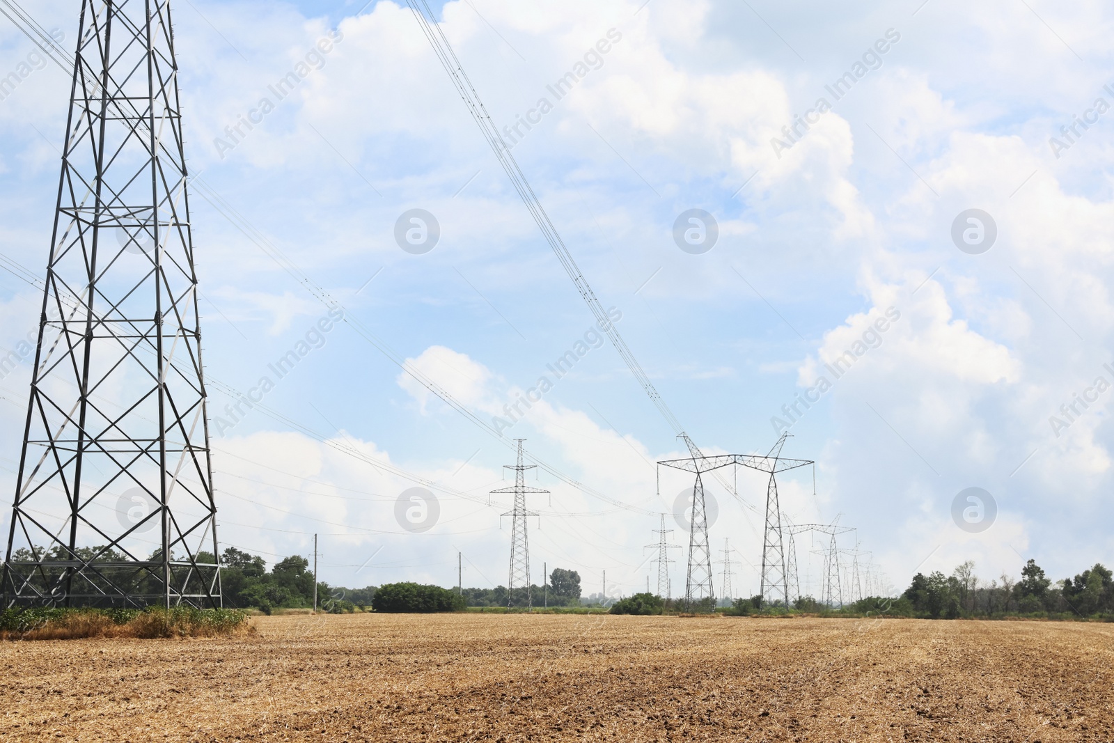 Photo of High voltage towers with electricity transmission power lines in field on sunny day