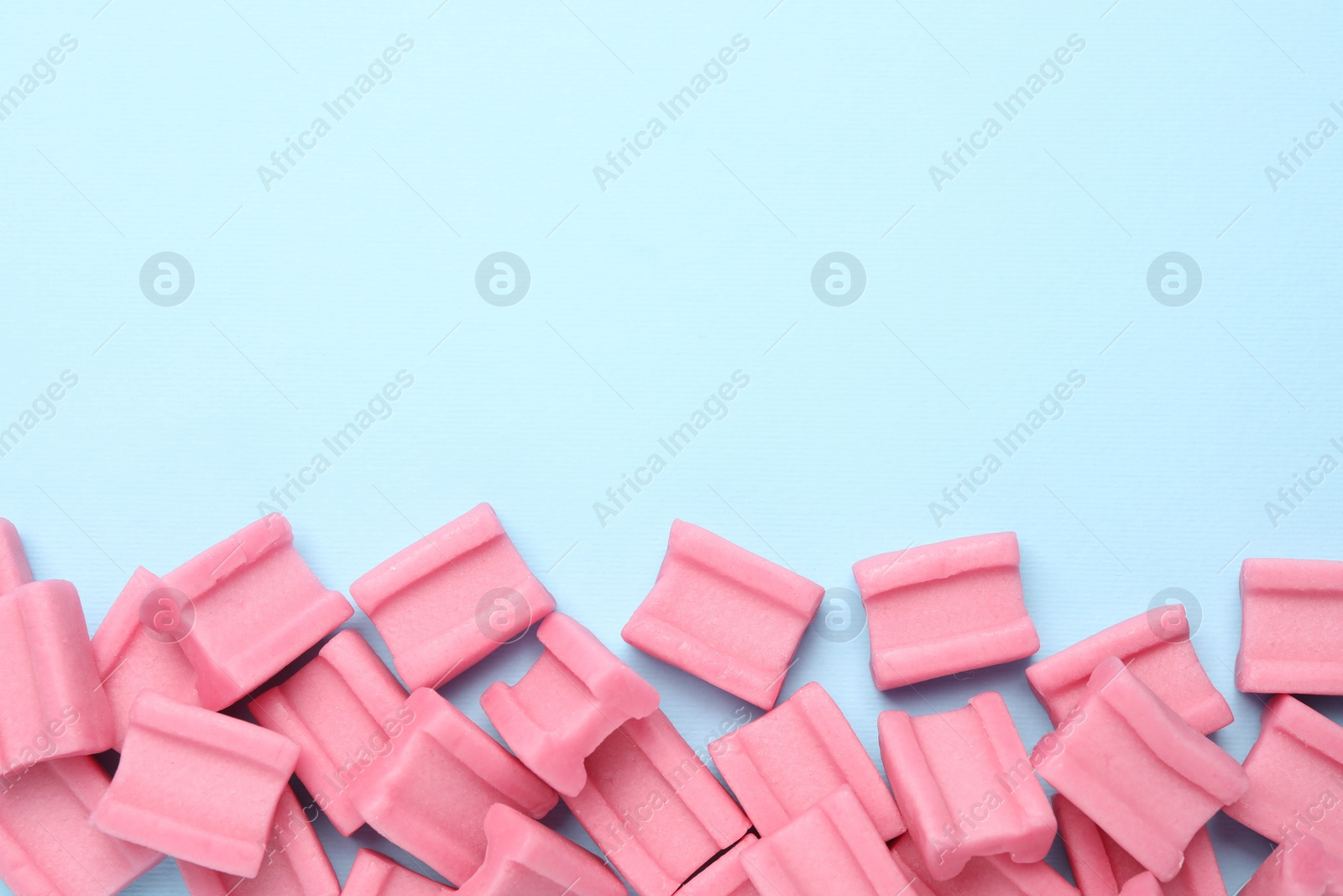 Photo of Tasty pink chewing gums on light blue background, flat lay. Space for text