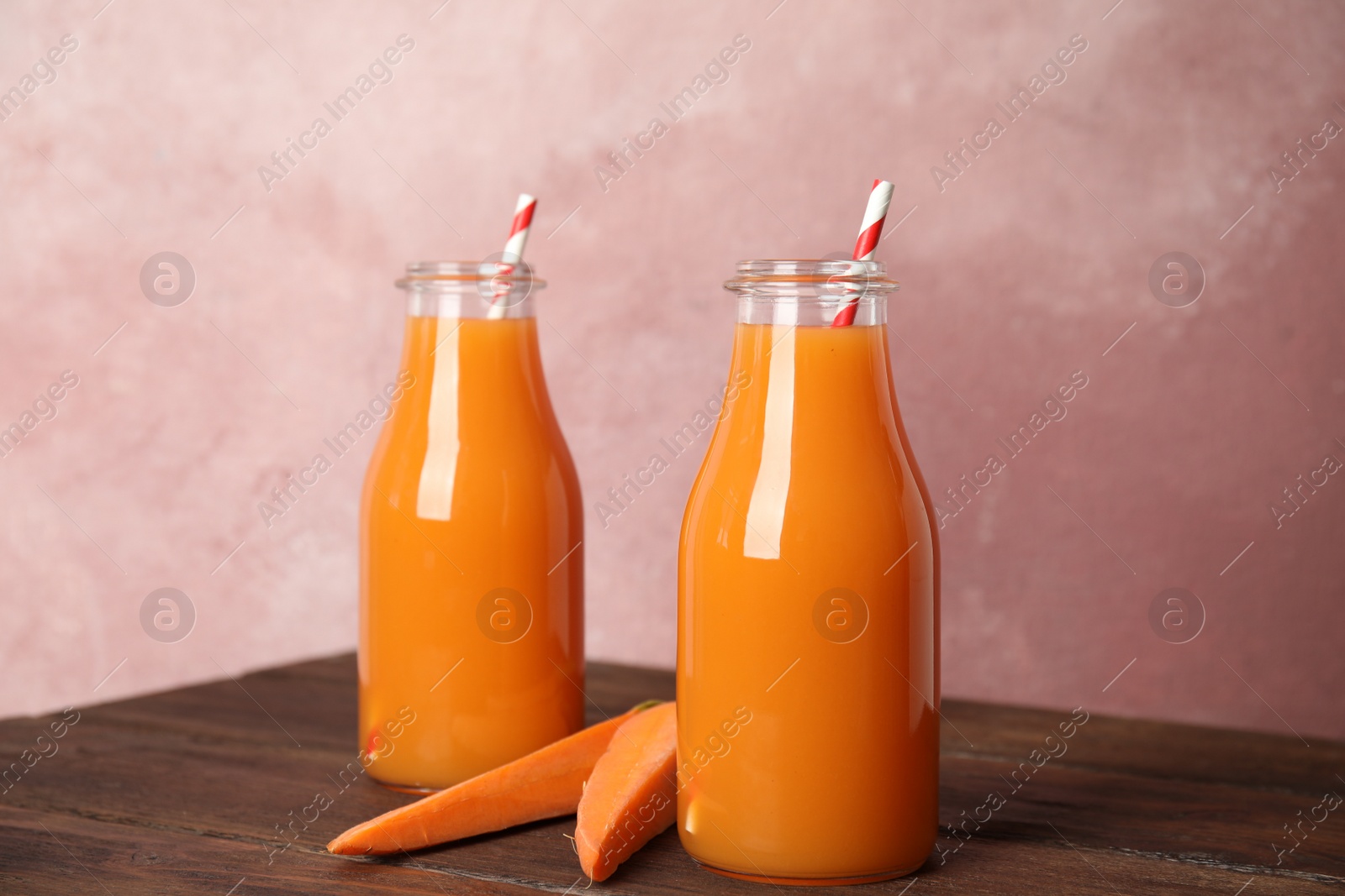 Photo of Freshly made carrot juice in bottles on wooden table