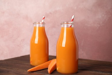 Photo of Freshly made carrot juice in bottles on wooden table