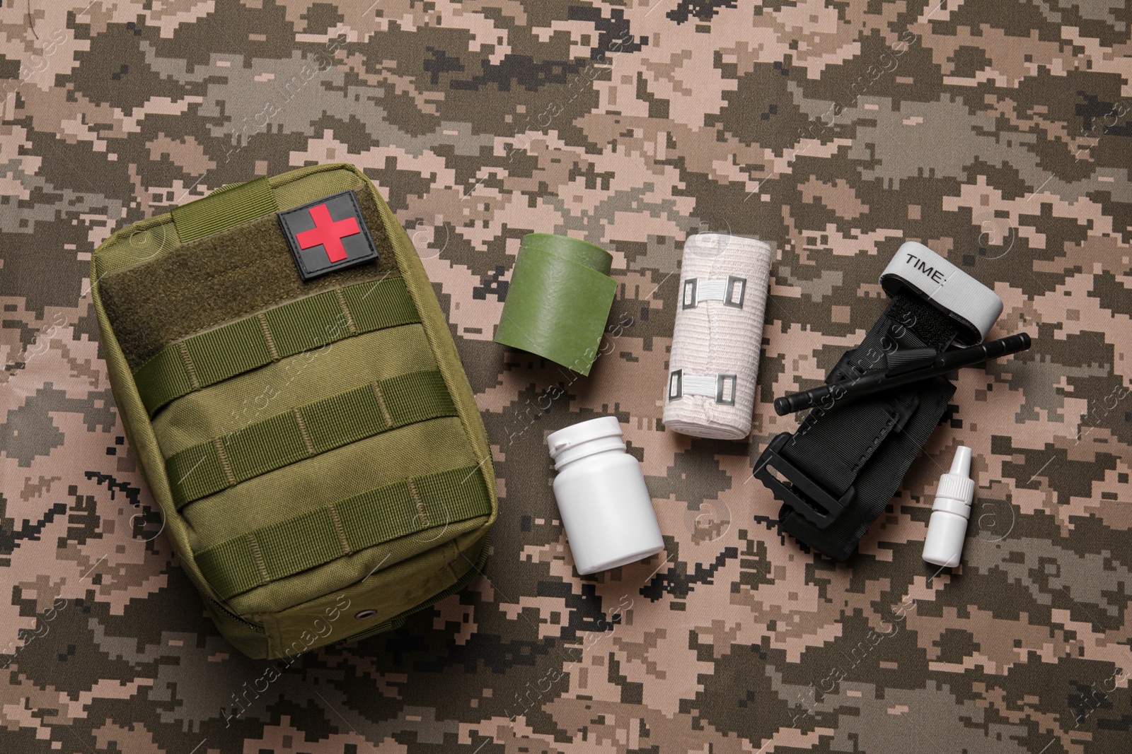 Photo of First aid kit with medical tourniquet, pills and bands on military fabric, flat lay