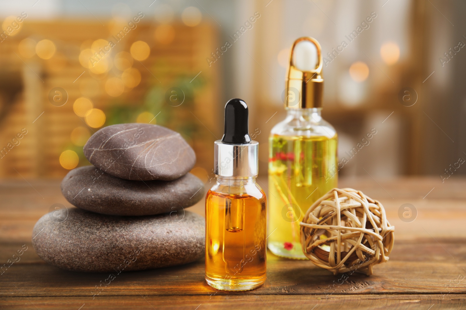 Photo of Essential oil, spa stones and decorative ball on wooden table against blurred lights