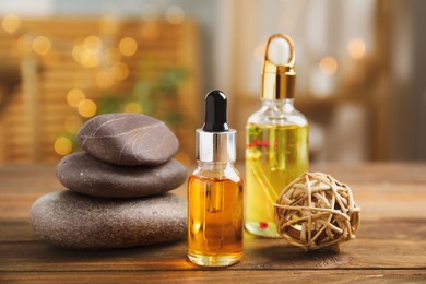 Photo of Essential oil, spa stones and decorative ball on wooden table against blurred lights