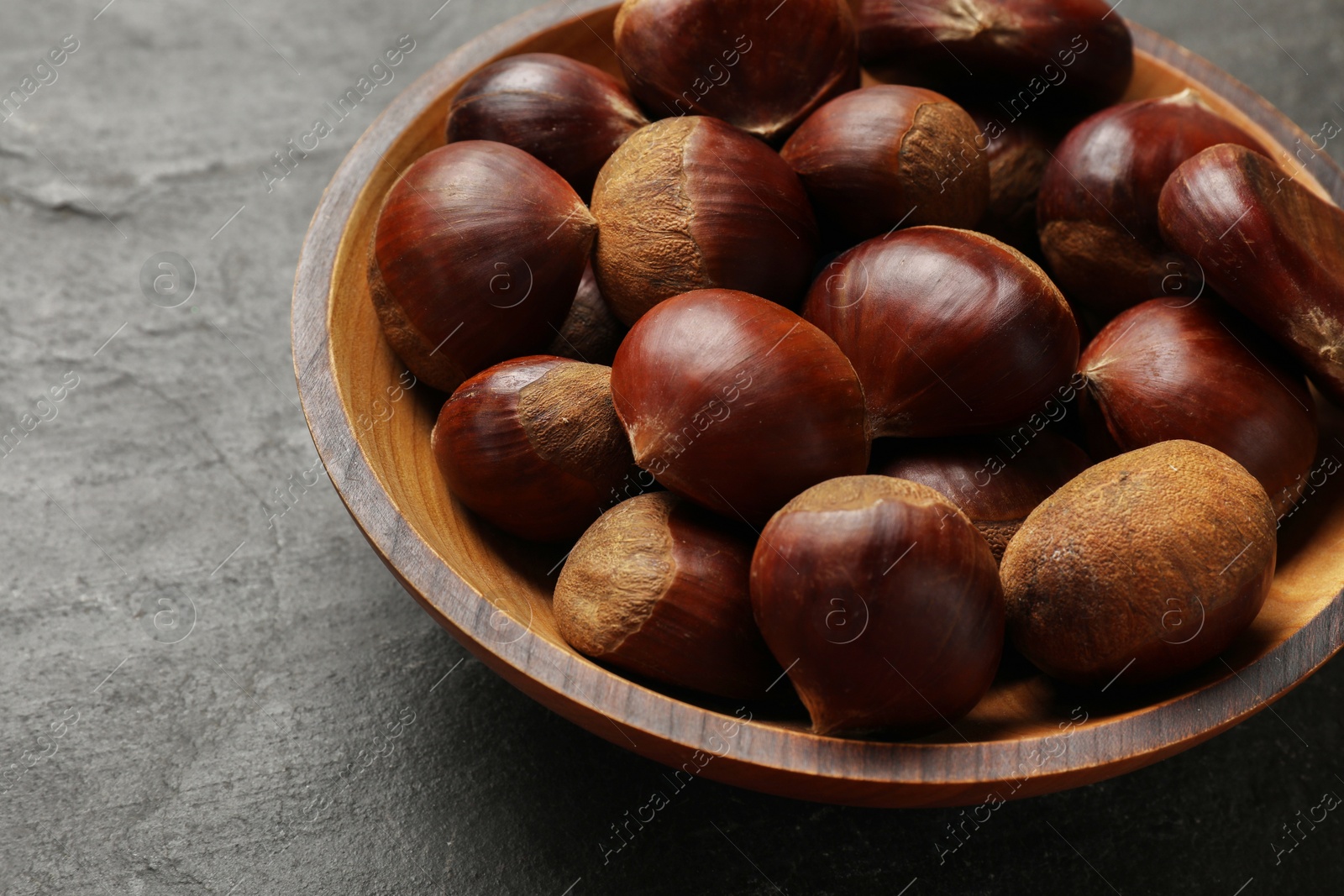 Photo of Roasted edible sweet chestnuts in bowl on grey textured table, closeup