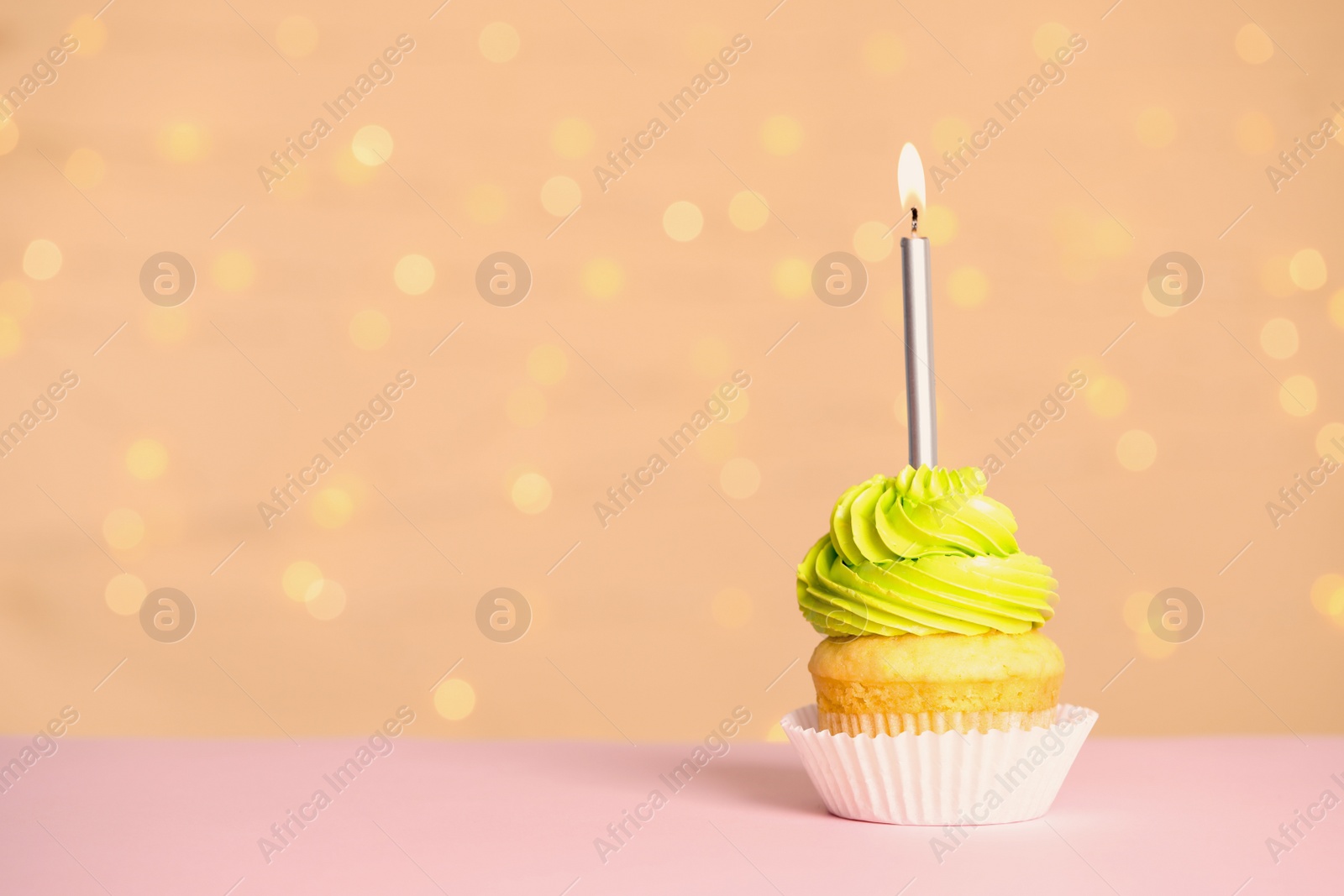 Photo of Birthday cupcake with candle on table against festive lights, space for text