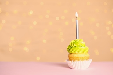 Photo of Birthday cupcake with candle on table against festive lights, space for text