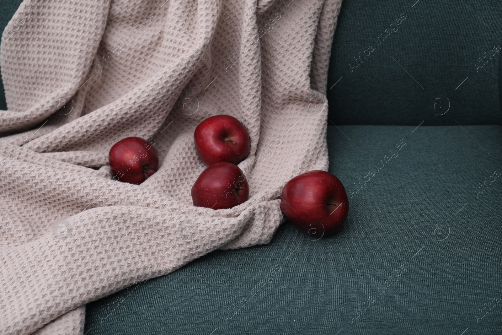 Photo of Red apples and beige blanket on green sofa