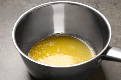 Photo of Saucepan with melting butter on grey table, closeup
