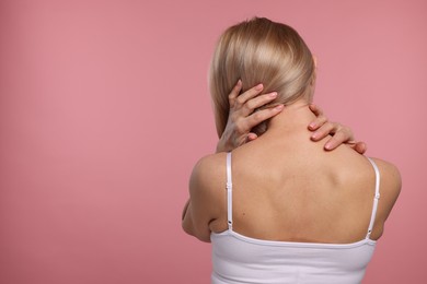 Photo of Woman suffering from pain in her neck on pink background, back view. Space for text