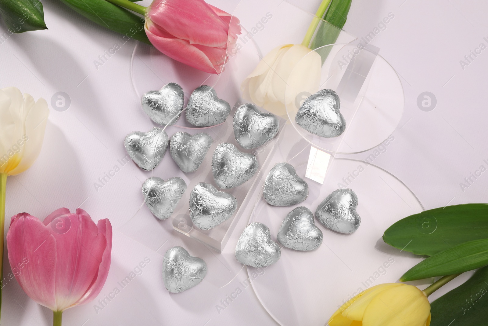 Photo of Heart made with delicious chocolate candies and beautiful tulips on white background, top view