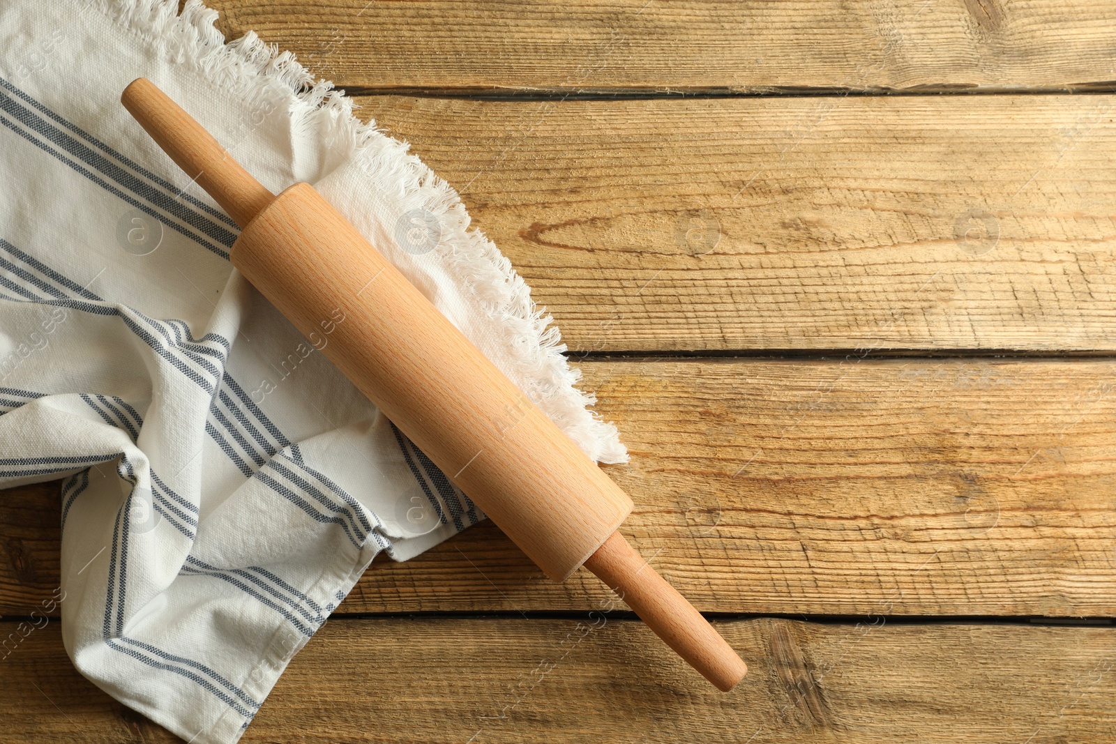 Photo of Rolling pin and kitchen towel on wooden table, top view. Space for text