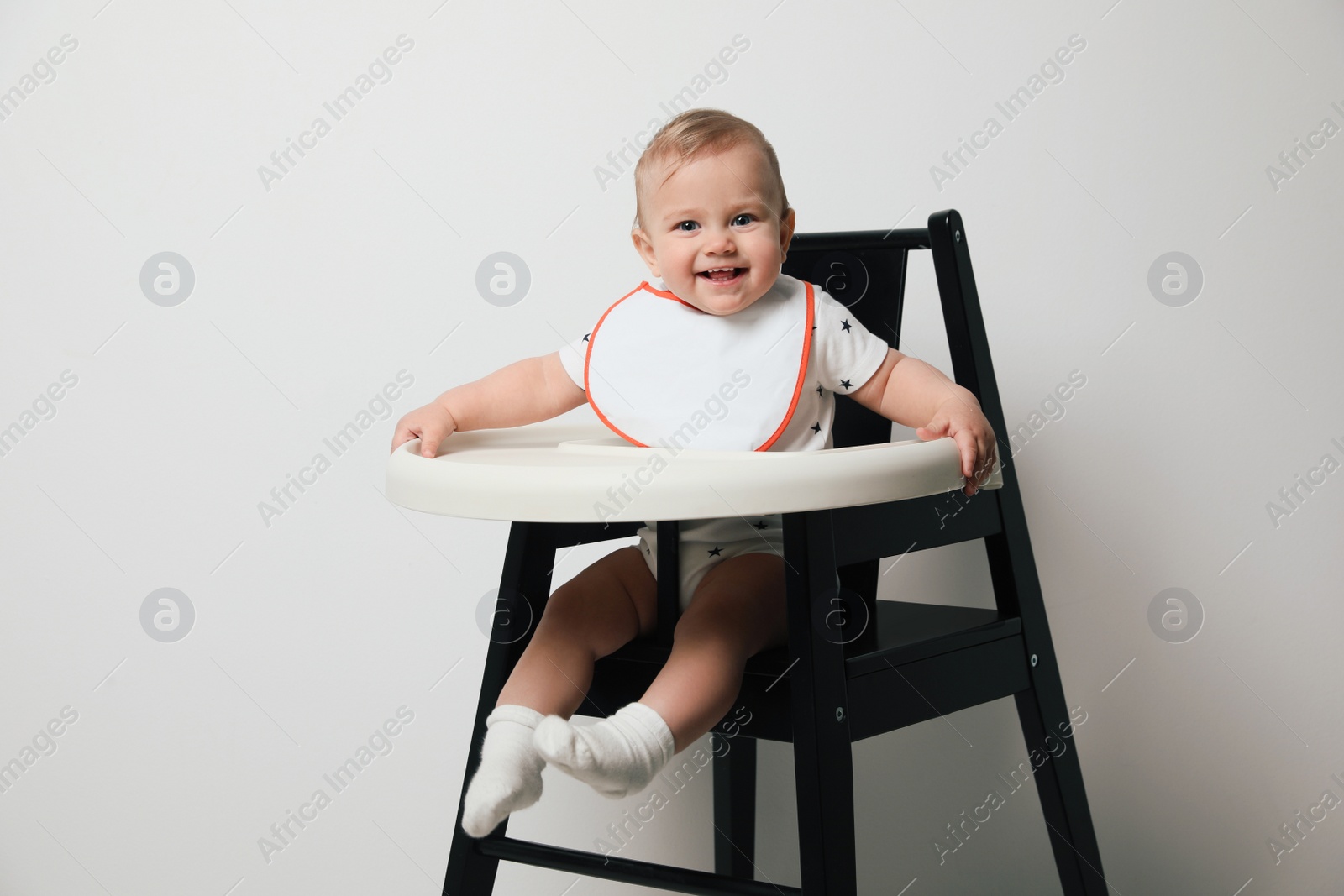 Photo of Cute little baby wearing bib in highchair on white background