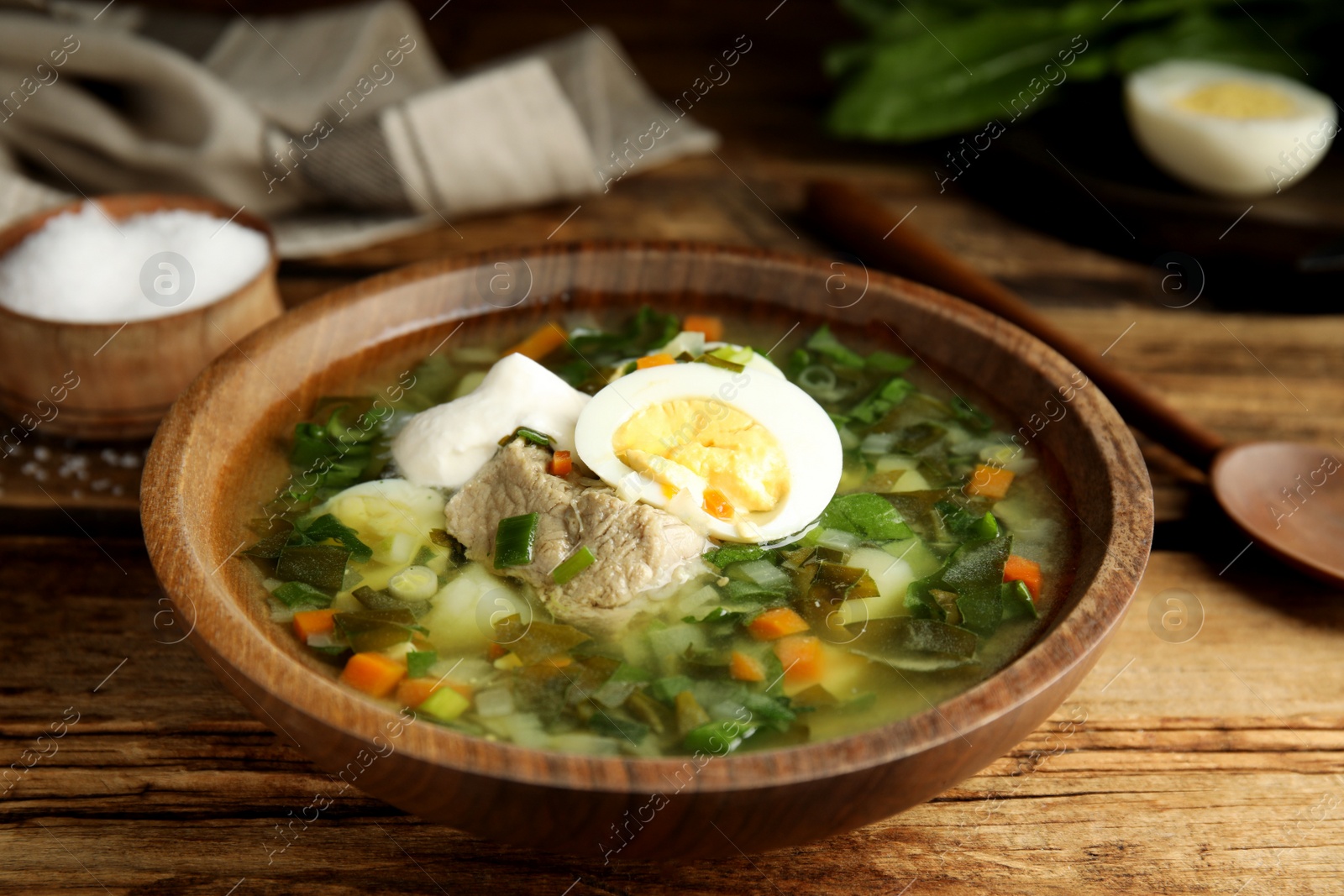 Photo of Delicious sorrel soup with meat and egg served on  wooden table, closeup