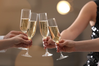 Photo of People clinking glasses of champagne against blurred background, closeup. Bokeh effect