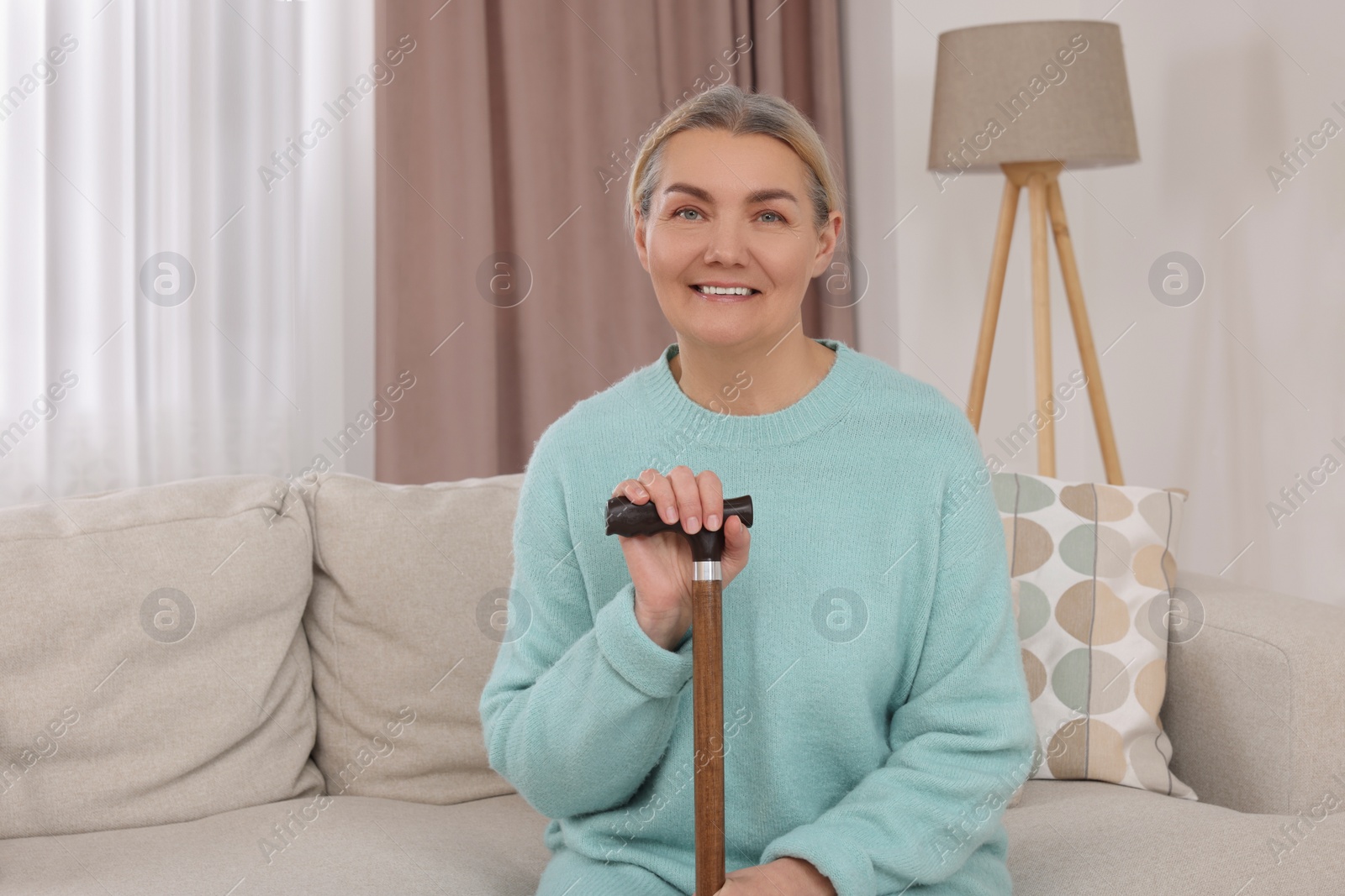 Photo of Senior woman with walking cane sitting on sofa at home