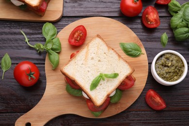 Photo of Delicious Caprese sandwich with mozzarella, tomatoes, basil and pesto sauce on wooden table, flat lay