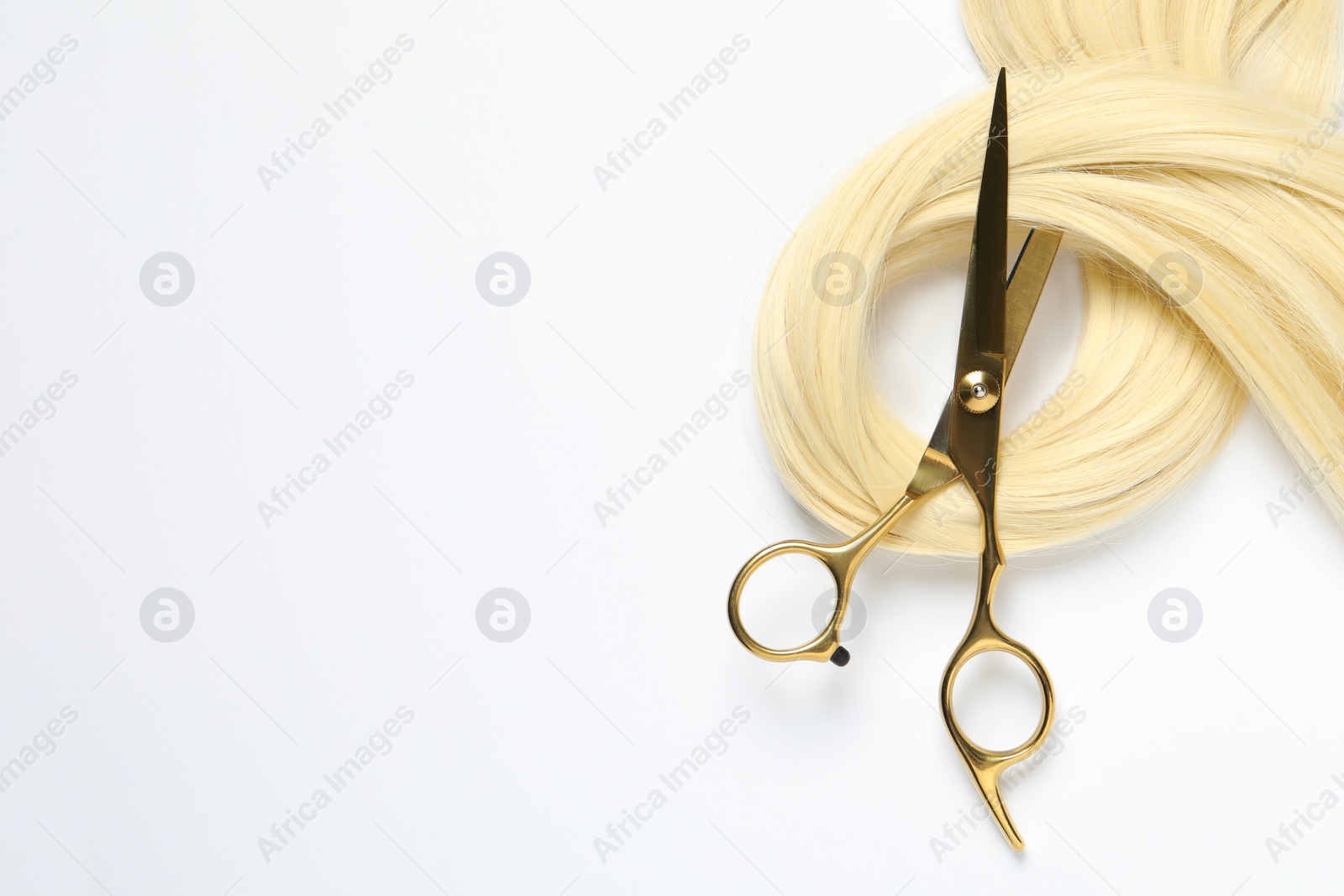 Photo of Professional hairdresser scissors with blonde hair strand on white background, top view