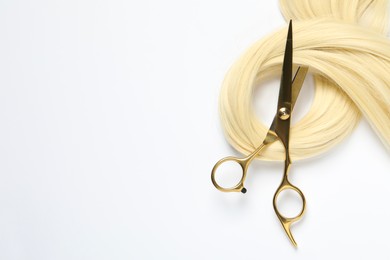 Photo of Professional hairdresser scissors with blonde hair strand on white background, top view