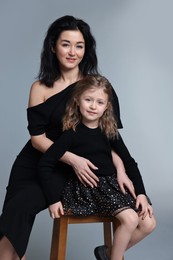 Photo of Beautiful mother with little daughter on stool against grey background