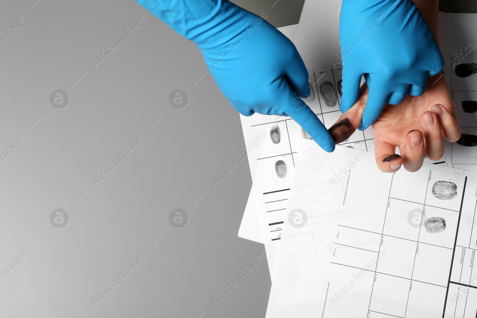 Photo of Investigator taking fingerprints of suspect on grey table, closeup. Space for text