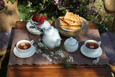 Photo of Beautiful spring flowers, freshly baked waffles and ripe strawberries on table served for tea drinking in garden