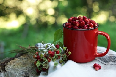 Photo of Mug and tasty wild strawberries on stump against blurred background. Space for text
