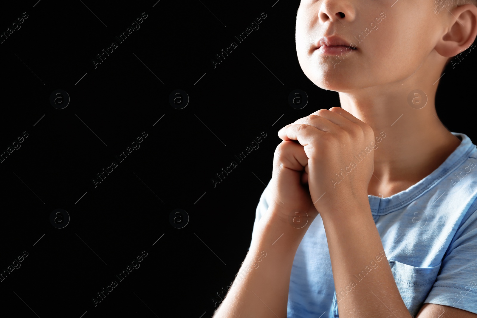 Photo of Little boy with hands clasped together for prayer on black background. Space for text