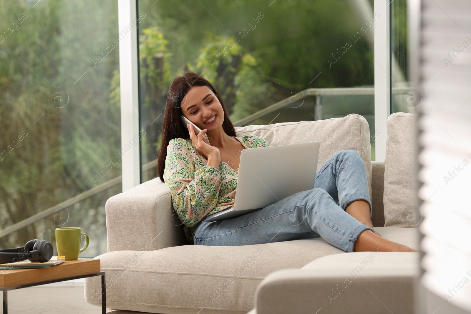 Photo of Young woman talking on phone while working with laptop at home