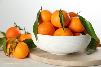 Photo of Fresh ripe tangerines with green leaves on white wooden table