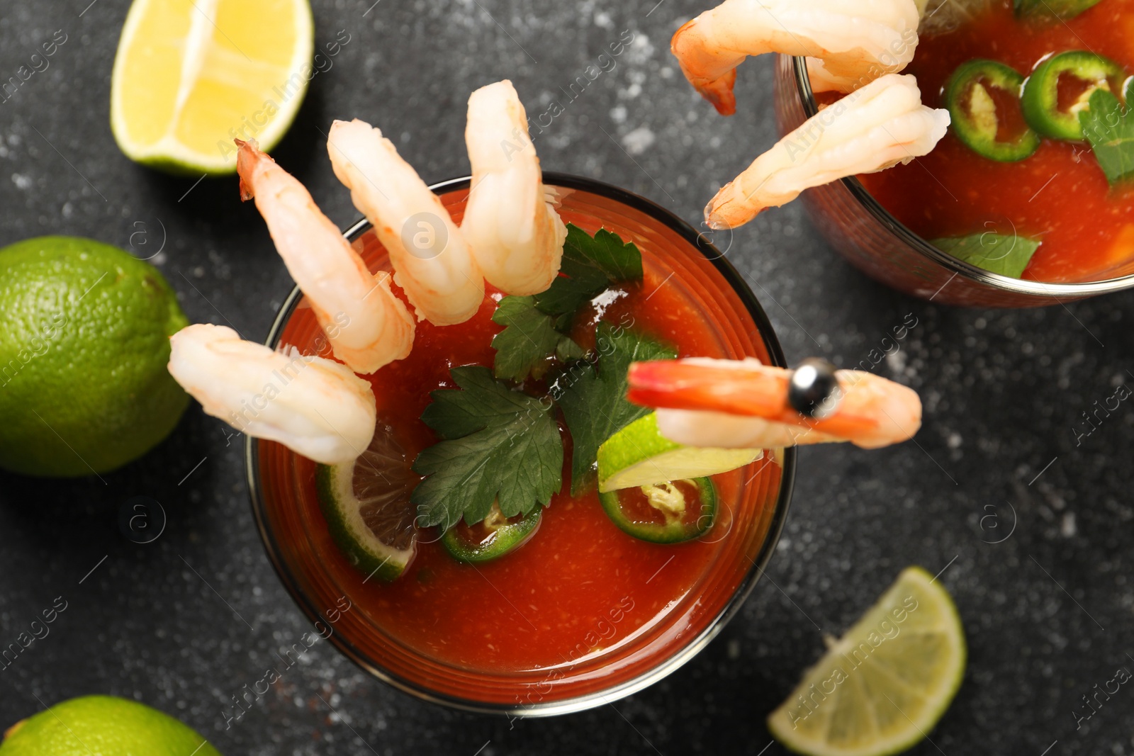 Photo of Tasty shrimp cocktail with sauce in glasses and limes on grey textured table, flat lay