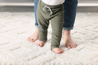 Photo of Mother supporting her baby son while he learning to walk on carpet, closeup