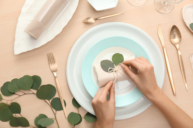 Photo of Woman setting table with green leaves for festive dinner, top view