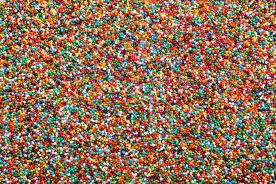 Photo of Bright colorful sprinkles as background, top view. Confectionery decor
