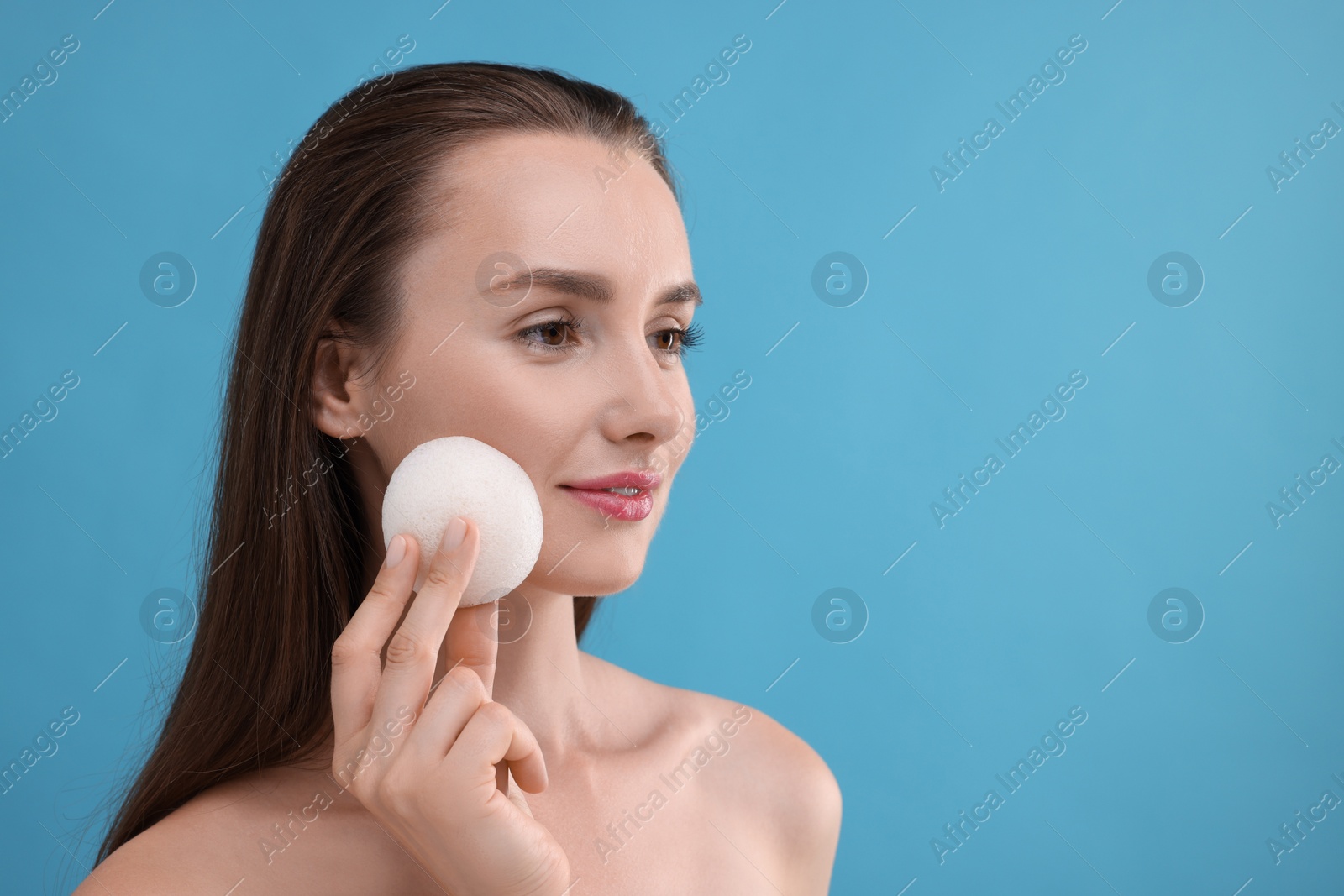 Photo of Young woman holding face sponge on light blue background. Space for text