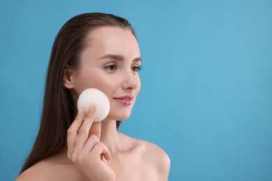 Young woman holding face sponge on light blue background. Space for text