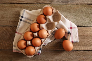 Raw chicken eggs with carton and napkin on wooden table, flat lay