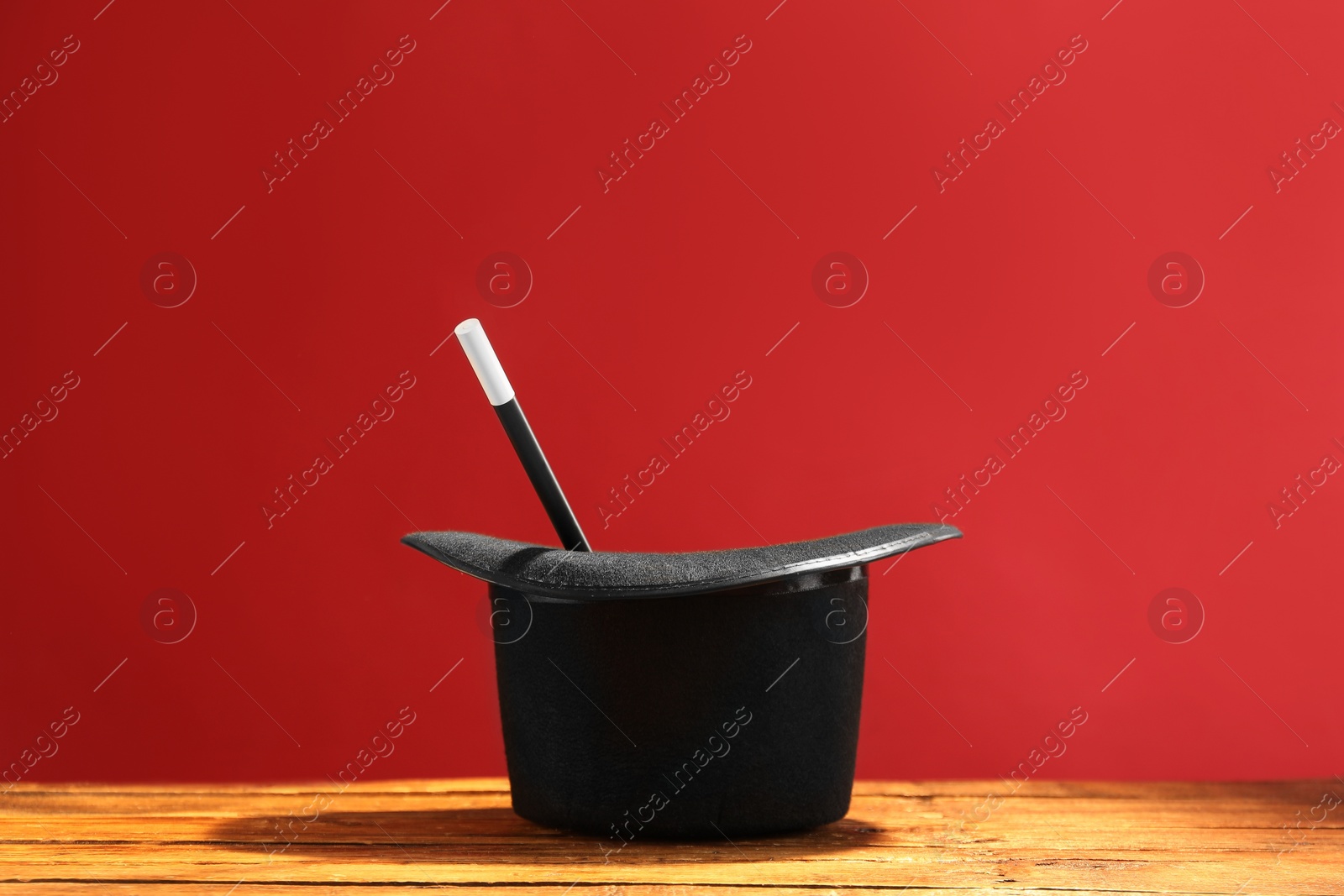 Photo of Magician's hat and wand on wooden table against red background