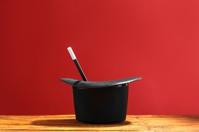 Photo of Magician's hat and wand on wooden table against red background