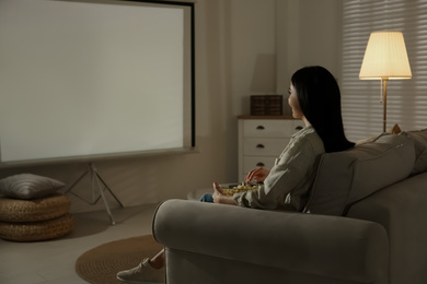 Photo of Young woman watching movie using video projector at home