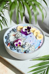 Photo of Delicious smoothie bowl with fresh fruits, blueberries and flowers on color textured table